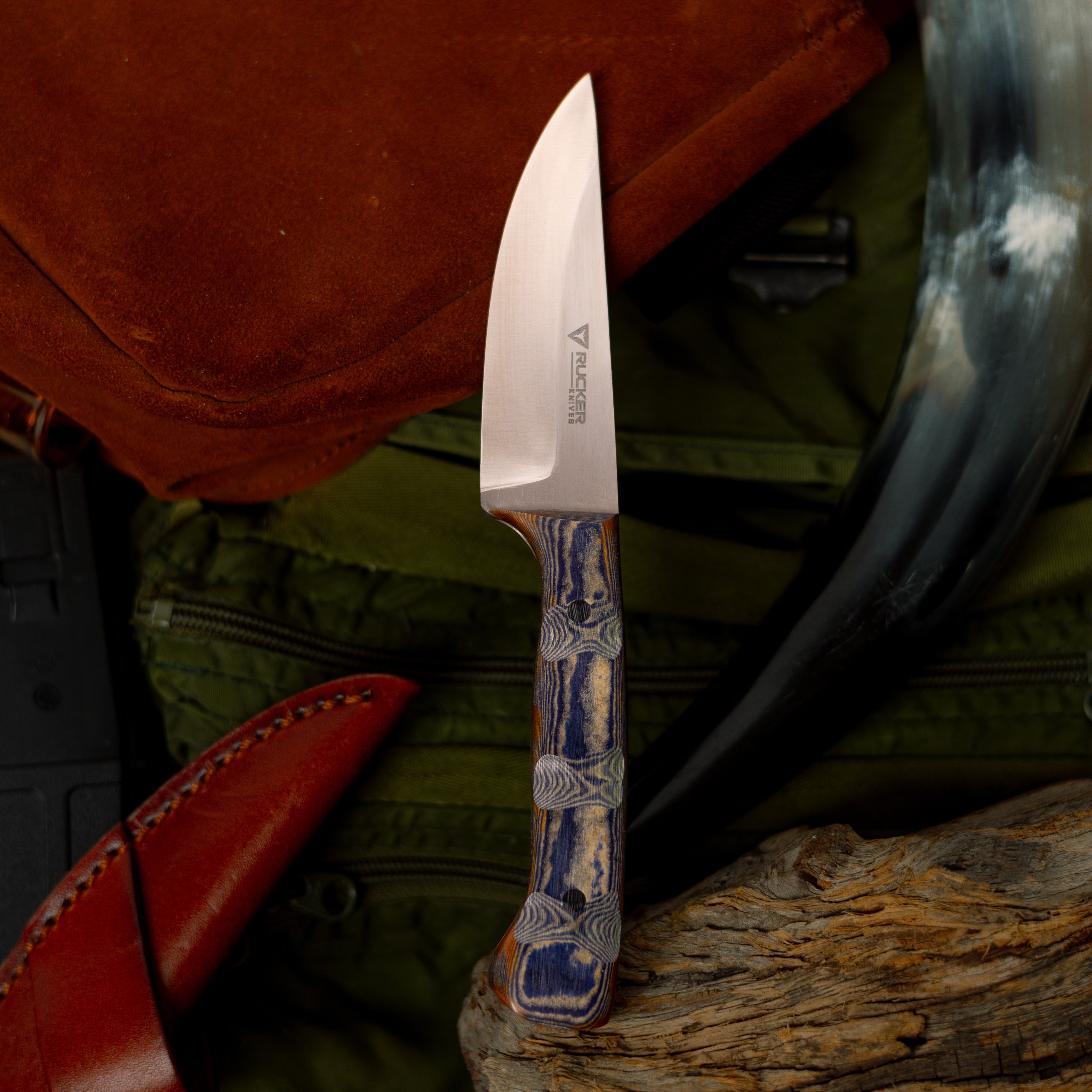 Rucker Knives Ridge Walk in a staged enviroment with buffalo horn, leather sheath, leather pouch, and greeen duffle bag in the background.