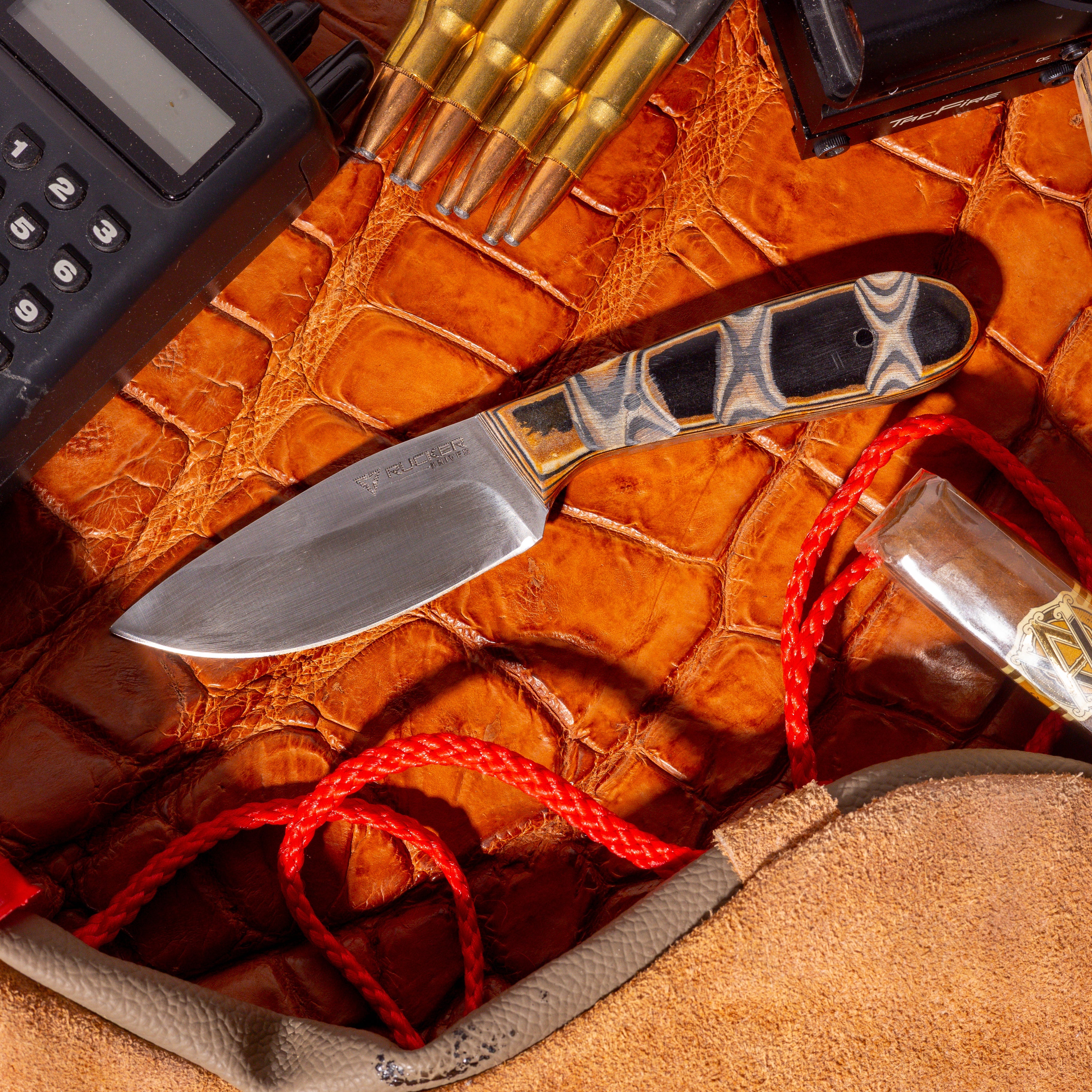 Rucker Knives White Tail knife in a staged enviroment with radio phone, cigar, alligator leather, and bullets in the scene.